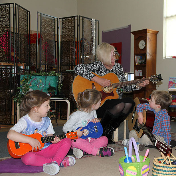 Photo of Liz playing guitar in front of three children