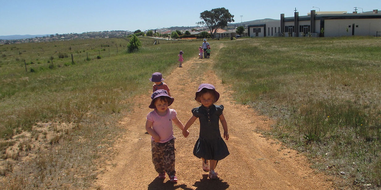Photo of children walking on a dirt path surrounded by grass